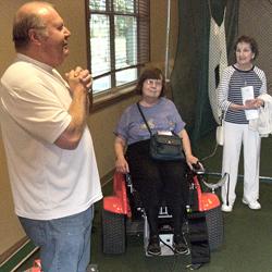 Roger Gatts demonstrating special cart for legless vets with help of audience member Marilyn Swartz.